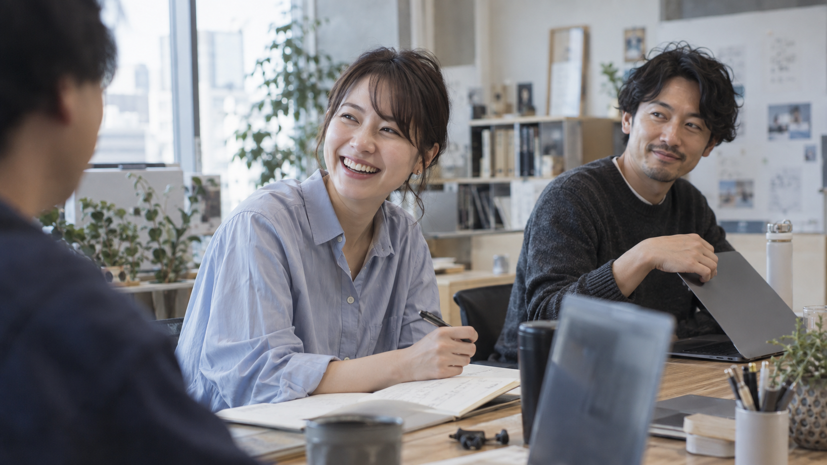 会話の相手に笑顔を向け、ノートを手に話を聞く女性と同席する人たち。