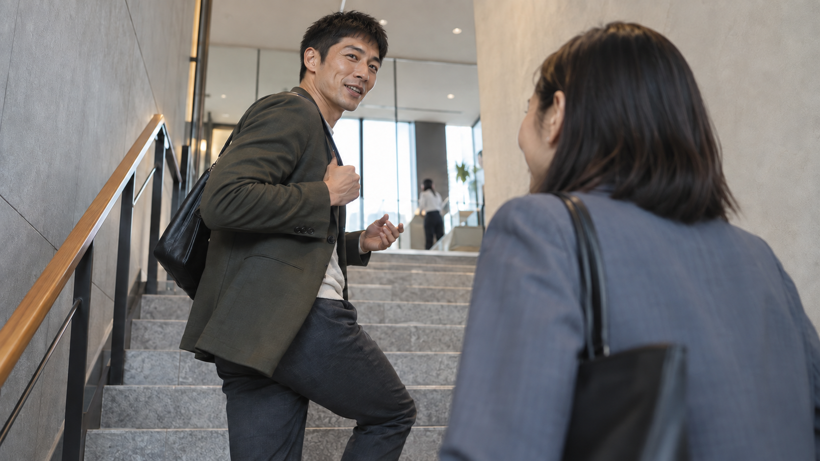 オフィスの階段を上りながら、振り返って同僚と話す男性。